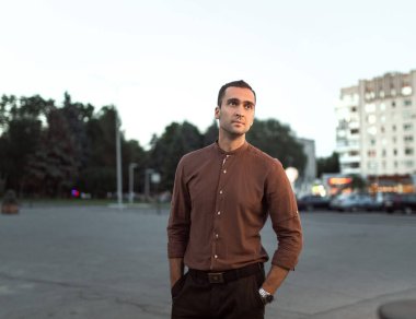 Tıraşsız, kahverengi gömlekli genç bir adamın portresi. Şehrin arka planında.