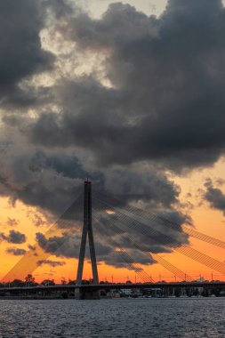 Letonya, Riga 'daki Daugava nehri ve Vansu ya da Askılık Köprüsü üzerinde muhteşem bir günbatımı. Renkli bulutlar ve sıcak tavan penceresi