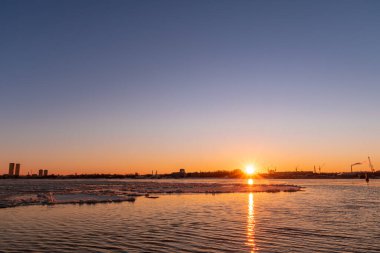 Riga Limanı 'nda sakin bir kış günü. Kısmen donmuş Daugava nehri ve arka planda Z kuleleri olan sanayi bölgesi.