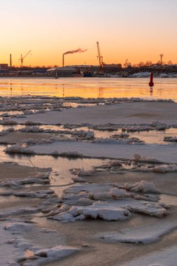 Riga Limanı 'nda sakin bir kış günü. Kısmen donmuş Daugava nehri ve arka planda Z kuleleri olan sanayi bölgesi.