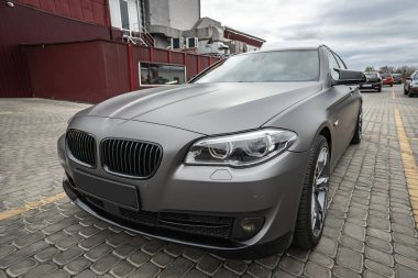 Predatory car headlight with blue lights and hood of powerful grey blue car sports car with matte grey paint and wheel
