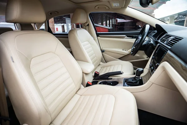 Araç içi lüks. Bej konforlu koltuklar, direksiyon, gösterge paneli, iklim kontrolü, hız göstergesi, ekran, ahşap süsleme ışığı