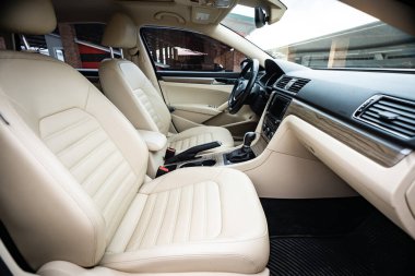 Araç içi lüks. Bej konforlu koltuklar, direksiyon, gösterge paneli, iklim kontrolü, hız göstergesi, ekran, ahşap süsleme ışığı