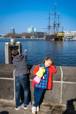 Amsterdam, Hollanda - 29 Mart 2022: Amsterdam 'daki NEMO bilim merkezi yakınlarında iki çocuk. Amsterdam Centraal İstasyonu yakınlarındaki deniz müzesi. Güneşli bir yaz gününde fütürist bir bina..