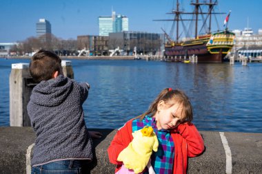 Amsterdam, Hollanda - 29 Mart 2022: Amsterdam 'daki NEMO bilim merkezi yakınlarında iki çocuk. Amsterdam Centraal İstasyonu yakınlarındaki deniz müzesi. Güneşli bir yaz gününde fütürist bir bina..