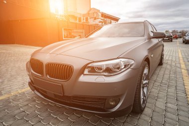 Predatory car headlight with blue lights and hood of powerful grey blue car sports car with matte grey paint and wheel