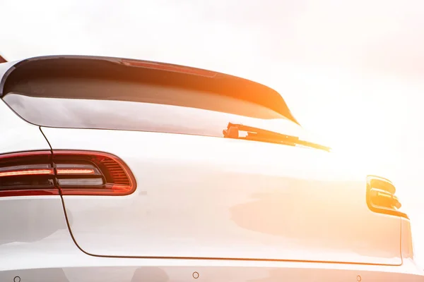 Back view part of white car parked on city pedestrian zone pavement on background of blurred silhouettes people walking along green sunny summer alley. Modern city lifestyle concept.