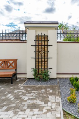 Arka ve ön bahçe kır evi bahçesi, çiçek açan bitki ve yeşil çimenler, kahverengi kaldırım ve turuncu tuğla duvar, arka planda her zaman yeşil ağaçlar, parktaki bakımlı peyzaj.