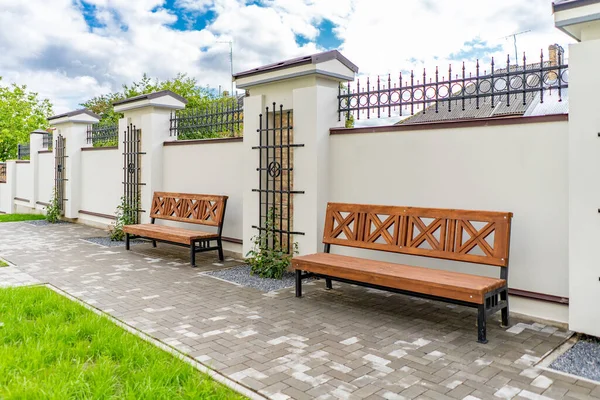 Arka ve ön bahçe kır evi bahçesi, çiçek açan bitki ve yeşil çimenler, kahverengi kaldırım ve turuncu tuğla duvar, arka planda her zaman yeşil ağaçlar, parktaki bakımlı peyzaj.