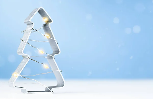 Açık mavi arka planda duran Noel ağacı şeklinde bir kurabiye kesicisi.