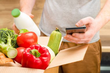 Elinde telefon ve bir kutu taze yiyecek olan bir adam.