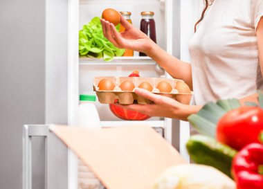 Kadın buzdolabına yumurta koyar.