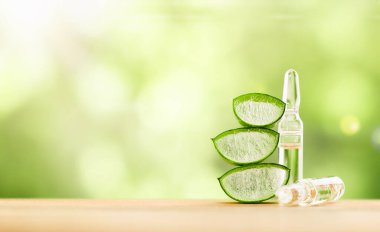 İki ampul sıvı ve ahşap bir masa üzerinde aloe parçaları.