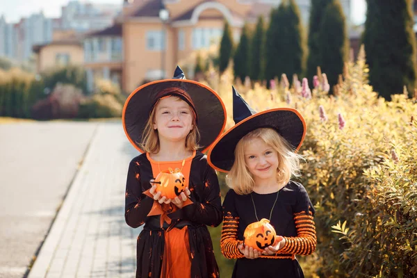 Two funny girls in Halloween costumes are holding jack o lanterns in their hands outdoors in autumn. — Stock Photo, Image