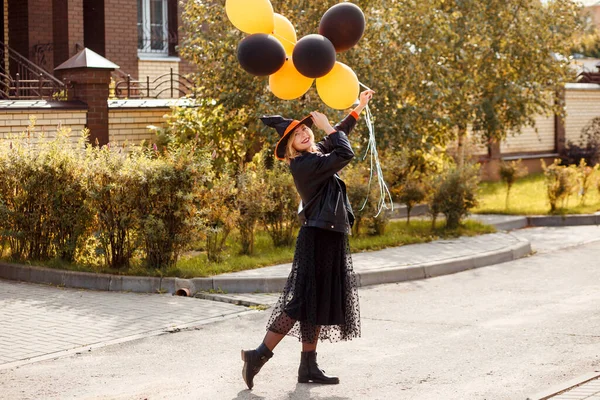 Retrato de mujer atractiva usando sombrero de bruja de Halloween y sosteniendo globos naranjas y negras. —  Fotos de Stock