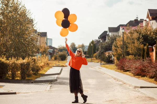 Привлекательная улыбающаяся женщина, одетая в оранжевый свитер и темную юбку с воздушными шарами в руках. — стоковое фото