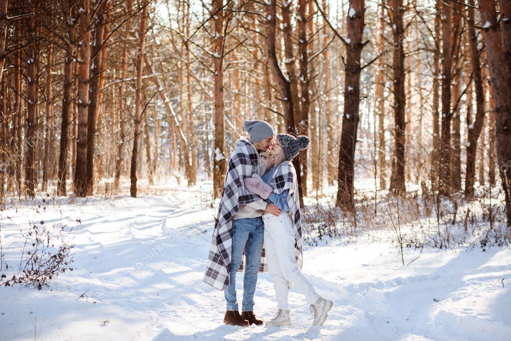 Cute loving couple spending time outdoors in winter forest, Christmas holidays.
