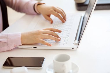 Dizüstü bilgisayarda yazan kadın elleri, ofis işyeri, bilgisayarın yanındaki akıllı telefon..
