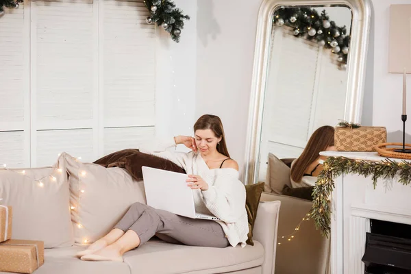 漂亮的女人正坐在家里的沙发上 用她的笔记本电脑在网上交流 圣诞节期间 — 图库照片