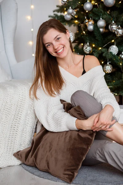 坐在圣诞树旁 穿着温暖的针织毛衣 面带微笑的女人的画像 — 图库照片