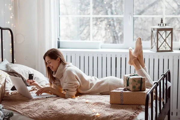 圣诞节期间，女人正躺在床上，用手提电脑和信用卡在网上购物. — 图库照片