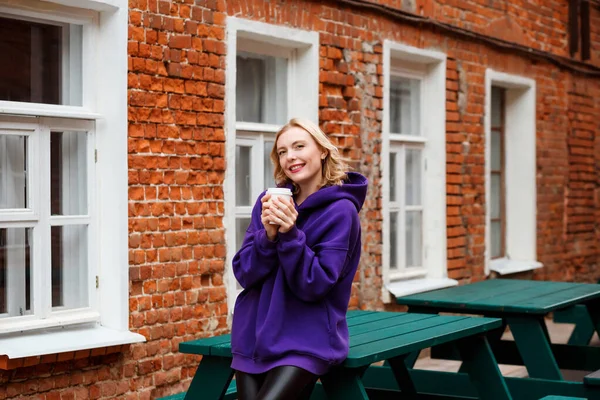 Счастливая Блондинка Фиолетовом Капюшоне Позирует Открытом Кафе Быстрого Питания Держа — стоковое фото