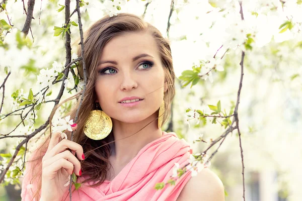 Hermosa novia elegante chica en una chaqueta rosa cerca del árbol con flores blancas con el viento en el pelo —  Fotos de Stock