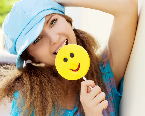 Beautiful young girl with a smile, with great candy in the hands of a Sunny day stands near the wall — Stock Photo, Image