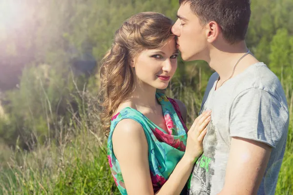 Kärleksfulla vackra par killar och tjejer i fältet walking man kyssas flickans panna — Stockfoto