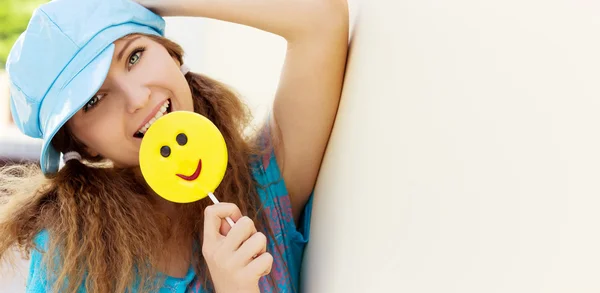 Krásná mladá dívka s úsměvem, s velkou candy v rukou za slunečného dne stojí u zdi — Stock fotografie
