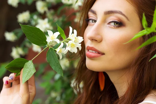 Joven hermosa chica sexy con un seductor labios más grandes con el pelo largo y rojo sentado en el Parque cerca del árbol Jasmine —  Fotos de Stock