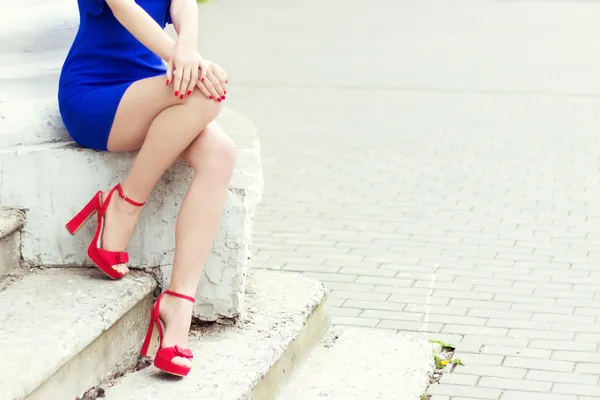 Menina pernas longas bonitas em sapatos vermelhos em vestido azul senta-se na cidade Fotografias De Stock Royalty-Free