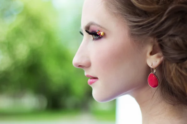 Beautiful young girl with red earring beautiful hair and make-up stands on the street in the city — Stock Photo, Image