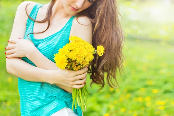 Hermosa chica en un día soleado de verano caminando en el jardín y mantiene dientes de león amarillos en las manos — Foto de Stock