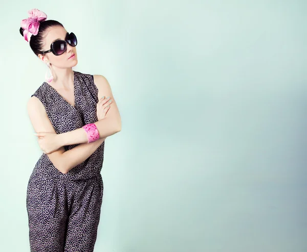 Schöne Retro-Mädchen mit Sonnenbrille und Schleife auf dem Kopf ist im Studio auf blauem Hintergrund — Stockfoto