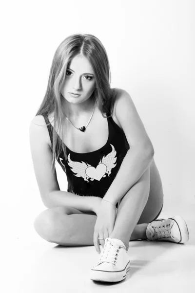 Beautiful young girl in jeans shorts and a sports Shoe sitting in the Studio on the white-blue background — Stock Photo, Image