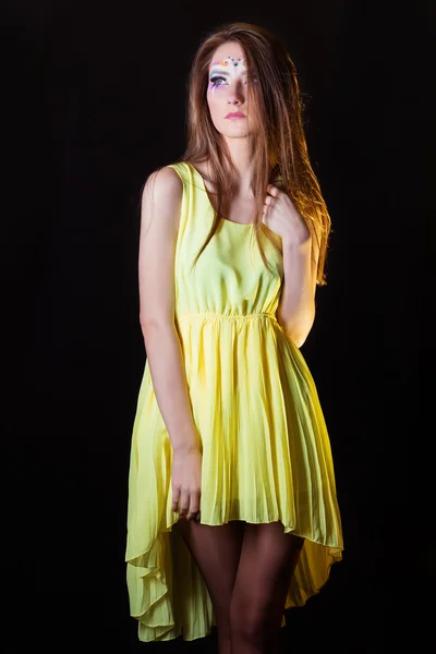 Beautiful young girl with art make-up is removed in the Studio on a black background in a yellow dress — Stock Photo, Image