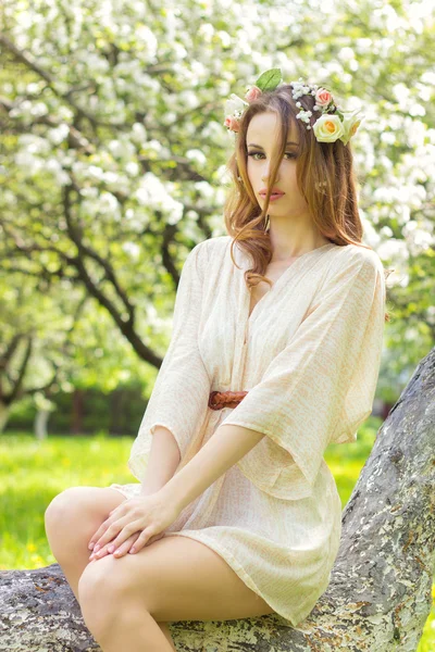 Piękna sexy dziewczyna z Rude włosy piękne składają się z kwiatami we włosach, siedzi na drzewie w bujnej sadu — Zdjęcie stockowe