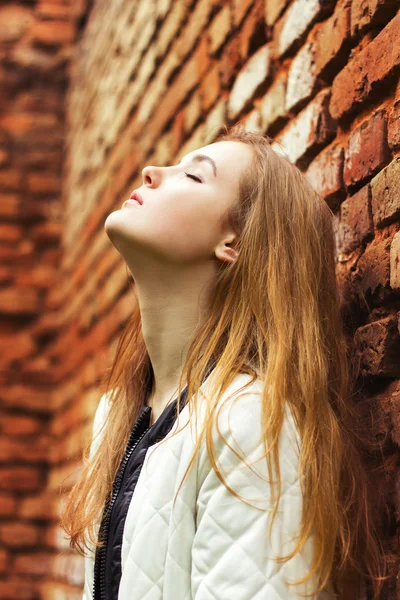 Bella giovane donna con lunghi capelli rossi si trova vicino alla strada rossa del muro in città — Foto Stock