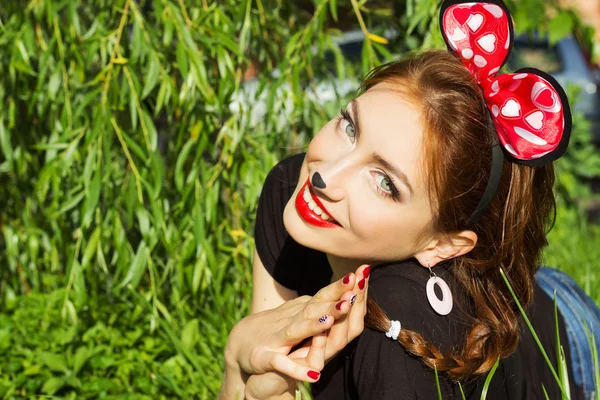 Hermosa chica feliz sonriendo en el traje de un ratón con un gran arco rojo abajo en la hierba en el Parque —  Fotos de Stock