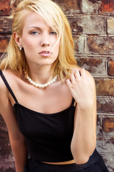 Retrato de una hermosa chica rubia con ojos azules contra la pared en las calles de la ciudad en un día de verano — Foto de Stock