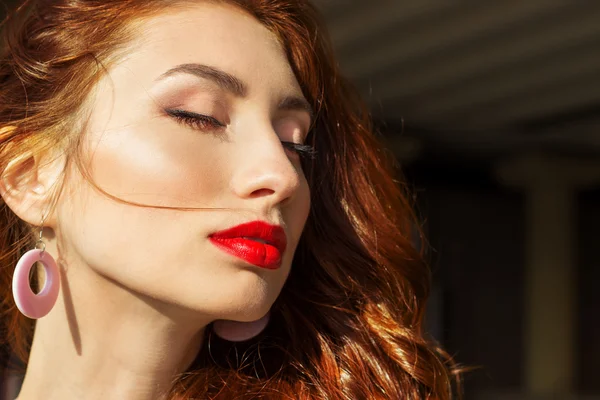 Beautiful sexy girl with red hair with big red lips with makeup in the city on a Sunny summer day — Stock Photo, Image