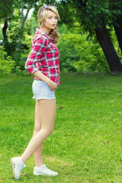 Beautiful sexy girl with white curly hair big lips with makeup stands in a clearing in the sneakers with shorts and shirt in a cage — Stock Photo, Image