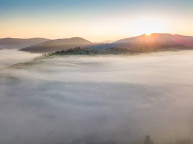 Sis şafakta dağların üzerine yayılır. Güneş ufuktan doğuyor. Sabah Ukraynalı Karpatlar. Hava aracı görünümü.