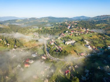 Bir dağ köyünün üzerinde ince bir sabah sisi. Sis dağların Ukrayna yamaçlarını kaplıyor. Hava aracı görünümü.