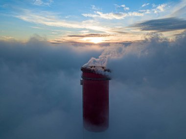 Gün batımında sislerin üzerinde bir termik santralin yüksek bacası. Hava aracı görünümü.