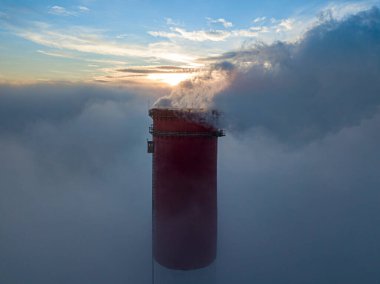 Gün batımında sislerin üzerinde bir termik santralin yüksek bacası. Hava aracı görünümü.