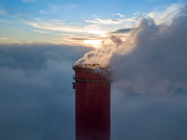 Gün batımında sislerin üzerinde bir termik santralin yüksek bacası. Hava aracı görünümü.