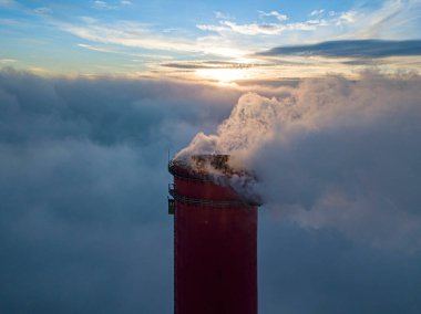 Gün batımında sislerin üzerinde bir termik santralin yüksek bacası. Hava aracı görünümü.