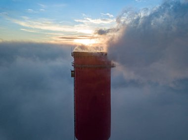 Gün batımında sislerin üzerinde bir termik santralin yüksek bacası. Hava aracı görünümü.